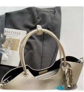 Détail du sac seau en cuir crème avec des poignées solides et un pendentif de sac