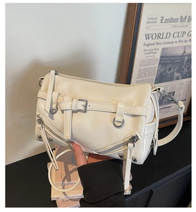 Close-up of cream bowling bag showing multiple zippers, buckles and metallic studs detail