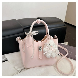 Détail du sac seau rose avec poignée en ruban et breloque lapin en peluche sur un banc