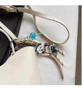 Détail d'un sac seau blanc crème avec une peluche de chien et des breloques stylées
