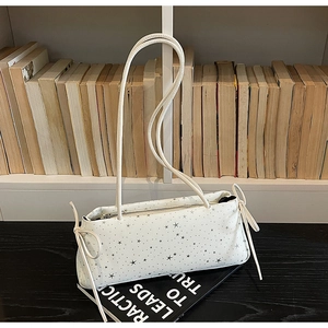 Close-up of a white baguette bag featuring silver star patterns and decorative bow ties