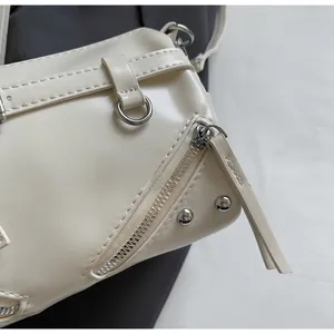 Detail view of smooth silver metal zippers and rivets on off-white PU shoulder bag