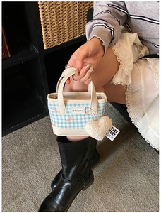 Detail of blue plaid bucket bag with pink bow pattern and plush heart pendant accessory