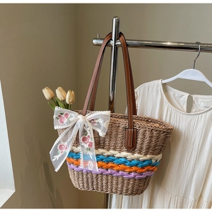Close-up of woven straw tote bag with colorful stripes, floral bow, and leather straps