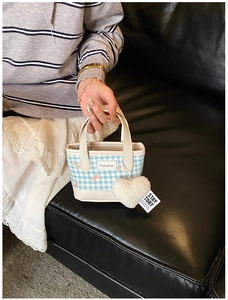 Close-up of blue plaid tote bag featuring pink bow pattern and plush heart charm