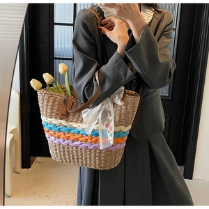Detailed close-up of woven straw tote bag with colorful patterns and leather handles