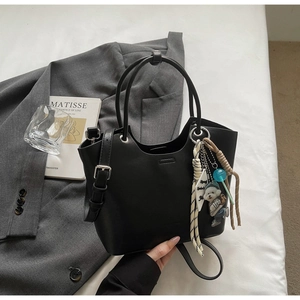 Vue détaillée du sac seau noir avec charm d'ours et corde tressée sur literie blanche