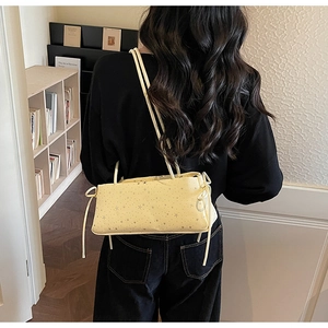 Detail of light yellow baguette bag featuring silver star patterns and bow-tie strap