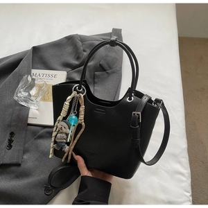 Détail du sac seau en cuir noir avec breloque chien en peluche et sucette attachée
