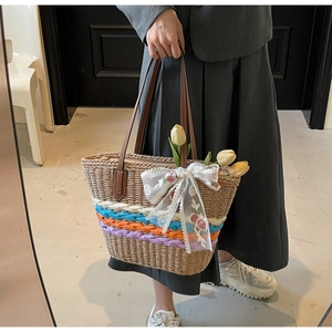 Detail view of woven straw tote bag featuring colorful base stripes and lace bow decoration