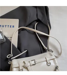 Detail of cream-white shoulder bag with double buckles and silver D-rings on a blazer