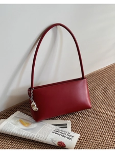 Detail of burgundy leather shoulder bag with decorative silver chain and lettered charm