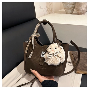 Détail du sac seau en cuir marron foncé avec poignée en foulard et breloque lapin