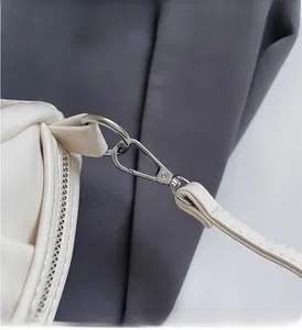 Macro detail of silver-toned metal hook hardware and strap on a white leather handbag