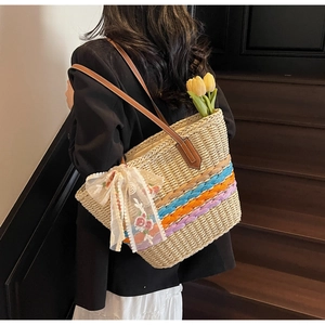 Detail of hand-woven straw tote bag with colorful stripes and lace flower bow
