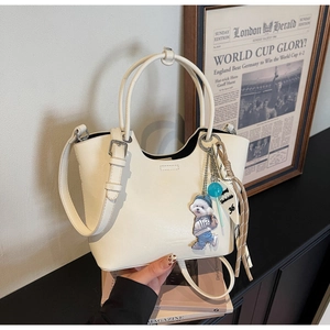 Détail du sac seau blanc cassé avec pendentif chiot et bandoulière réglable sur bois
