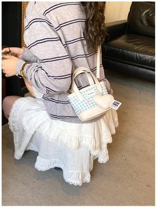 Detail of blue plaid mini bucket bag featuring a large white plush heart charm