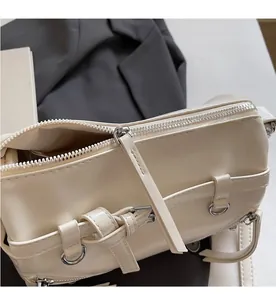 Close-up of smooth silver zipper and leather tassel detail on beige shoulder bag