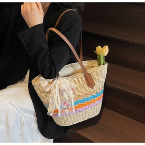 Detail of hand-woven straw tote bag with colorful stripes and white lace flower scarf