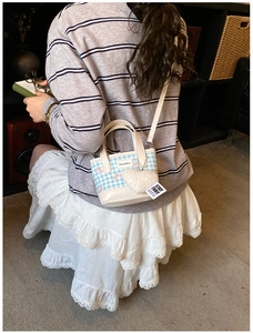 Detail of blue plaid bucket bag with heart charm and bow print on a model outfit