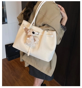 Detail of white lychee leather tote bag featuring a cute teddy bear charm with a knit hat