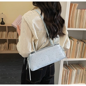 Detail of light blue leather baguette bag featuring silver star print and side drawstring