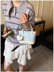 Detail of blue plaid mini tote bag with pink bow accents and plush heart charm pendant