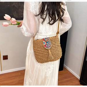 Detail of bohemian straw bag featuring colorful bead embroidery and long fringe tassels