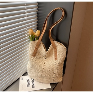 Detail showing hand-woven straw texture and brown leather strap of a beige tote bag