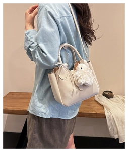 Détail du sac seau crème avec breloque lapin en peluche et texte embossé sur cuir synthétique