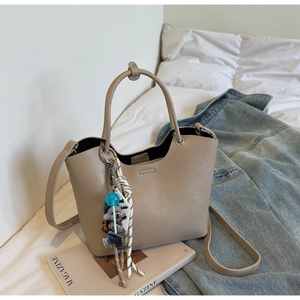 Détail d'un sac seau en cuir beige avec breloque ours sur fond de magazine