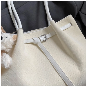 Detailed weave pattern of a beige tote bag with buckle and plush bear pendant