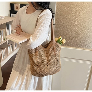 Detail of woven straw tote bag featuring brown leather shoulder straps and V-shaped texture