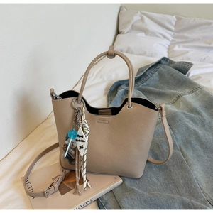 Détail du sac seau en cuir beige avec pendentifs décoratifs et pompon rayé