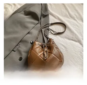 Detail view of brown quilted bucket bag with silver chain strap and drawstring closure