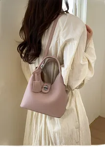 Detail view of a pink litchi grain leather bucket bag worn by a model in a natural setting