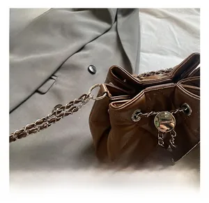 Detailed close-up of brown quilted bucket bag with silver metal chain and round buckle