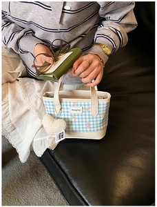 Detail of a mini plaid tote bag with heart charm on a black leather sofa with props