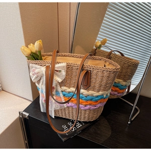 Detail of hand-woven straw tote bag with colorful stripes and lace bow on a black surface