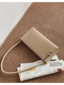 Detailed shot of beige leather underarm bag with silver crescent charm on woven mat