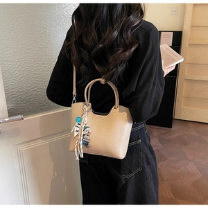 Détail d'un sac seau beige avec un charmant pendentif ours et un foulard en soie rayé chic