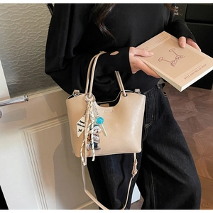 Détail d'un sac seau beige avec un charm d'ours mignon et des pendentifs décoratifs