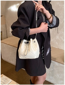 Detailed view of white quilted bucket bag with chain strap worn with a black blazer
