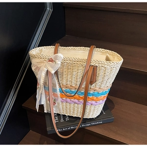 Close-up of woven straw tote bag featuring colorful stripes and white lace bow detail