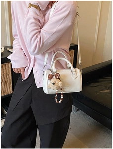 Close-up of white leather Boston bag with plush bear charm and fashion text detail