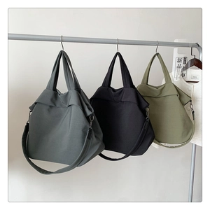 Trois sacs cabas en nylon gris, noir et vert olive suspendus sur un support en métal