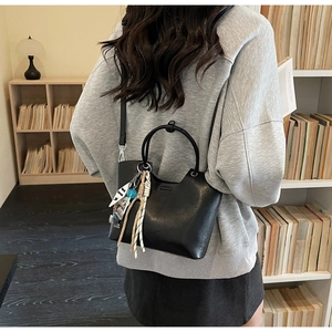 Détail d'un sac seau noir avec poignée métallique et breloque ours dans une bibliothèque cosy
