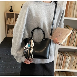 Détail d'un sac seau en similicuir noir avec sangle tissée dans un décor de bureau