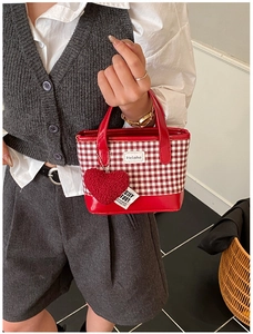 Close-up of red checkered mini bucket bag with heart pendant and brand logo detail