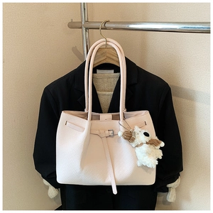 Detail of light pink woven tote bag featuring a metal buckle and plush puppy keychain